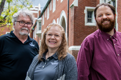 Joe Lyle, Frances Clark, and Austin Pryor stand together in front of a brick building.